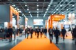 © BUTET - Blurred image of a bustling trade show floor with attendees walking along a vibrant orange carpet