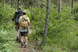 © pressmaster - Middle aged man and boy hiking together through forest trail carrying backpacks and fishing rods, walking side by side surrounded by dense green trees