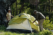 © pressmaster - Middle aged man and teenage boy setting up tent together in forested outdoor area, preparing camping site surrounded by trees and natural landscape