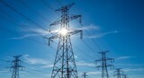 Silhouetted power transmission towers and lines against a vibrant blue sky with a radiant sunburst. Symbolizes energy, modern infrastructure, and power distribution.