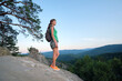 © bilanol - Hiker woman standing on mountain footpath enjoying evening nature during her travel on wilderness trail. Lonely female traveler traversing high hilltop route. Healthy lifestyle concept