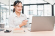 © kenchiro168 - Young Asian woman white shirt sitting at desk smiling holding pen pointing at digital tablet working on laptop modern office natural light professional confident