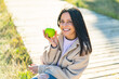 © luismolinero - Young woman at outdoors holding an apple with happy expression
