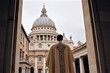 A Catholic priest wearing liturgical vestment arriving on the courtyard of a grand basilica to lead a congregation of faithful thru prayers, hymns, and scripture readings in a Sunday worship service.