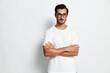 © SHOTPRIME STUDIO - Confident young man with glasses standing with arms crossed, wearing a white t-shirt, looking at the camera against a solid light background, studio portrait style.