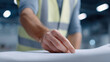© Nakarin - Male engineer in safety vest pointing at blueprint with focus on hand in industrial workspace with blurred background