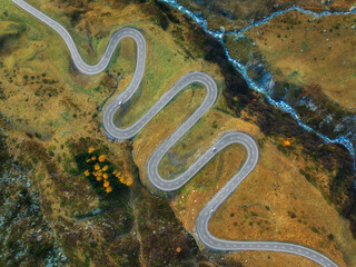 Wall Mural - aerial view of winding mountain road, river in alpine valley at sunset in autumn. top drone view of 