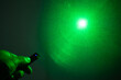 © JUN LI - A person's hand holding a remote with a glowing blue light and a green laser beam pointing upwards in a hazy atmosphere.