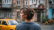 © perfectlab - Young woman standing on urban street in front of weathered apartment buildings and parked yellow car