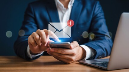 Businessman using a smartphone to check email notifications for marketing, communication, and business, with laptop on desk