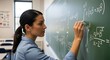 © StockBlend - Woman writing math equations on a chalkboard in a classroom with natural light source
