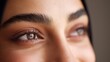 © tao - Close-up of beautiful brown eyes on a smiling woman with perfect eyebrows and eyelashes, looking directly at the camera, showcasing flawless skin under soft natural light.