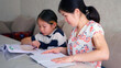 © chekart - A woman helps a little girl with her homework. A single mom and her daughter are doing their homework. A school textbook and a notebook