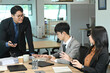 © Stella 16 - A group of people are sitting around a table in a business setting. One man is standing and talking to the group.