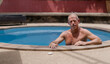 © Tj - Relaxed senior man enjoying summer vacation while lounging in a private home swimming pool, embracing a healthy and active lifestyle during retirement, surrounded by tranquil blue water
