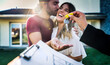 © Davide Angelini - Happy millennial couple receiving keys from realtor, purchasing real estate - Family meeting with real estate agent - New house and real estate concept