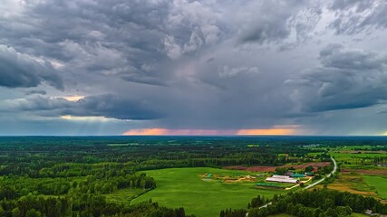 Wall Mural - Dark rain streaks down and light dance across hills and fields under shifting cloud cover with orange golden sky behind light rays