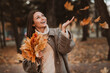 © deagreez - Young woman enjoying autumn park with colorful leaves in hand, portraying a cheerful and stylish seasonal outdoor moment