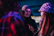 © qunica.com - Three friends wearing winter clothing converse warmly under festive lights, enjoying a chilly evening.