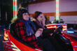 © qunica.com - Two friends share a playful moment on bumper cars during a lively winter celebration. Colorful lights and joyful expressions highlight the season's festive spirit.
