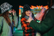© qunica.com - Young friends enjoying festive moments together outdoors during winter, illuminated by colorful lights.