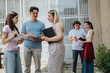 © qunica.com - Young adults discussing and engaging in educational collaboration while holding books and notebooks in an outdoor setting, emphasizing teamwork, academic goals, and positive interaction among peers.