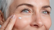 © Marut - Anti aging cream being gently applied to smooth skin near eye of mature woman with light eyes and white hair, showing care and skin rejuvenation