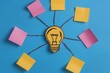 © Tati - Creative brainstorming concept with lightbulb and colorful sticky notes on blue background.