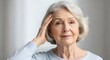 © helga - Thoughtful senior woman gently touching her temple, portrait against a soft, neutral background. A serene and contemplative expression conveys wisdom and inner peace.