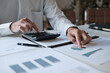© mojo_cp - Administrative staff reviewing company budget report with calculator, document stack and focus at office desk
