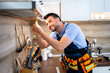 © Marko - Man repairs kitchen light fixture while smiling in modern apartment