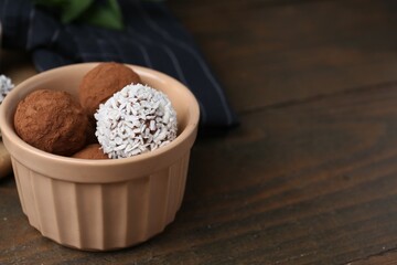 Wall Mural - Delicious homemade candies with cocoa powder and coconut flakes in bowl on wooden table, closeup. Space for text