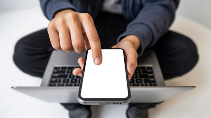 Close-up of person using smartphone with blank white screen while sitting with laptop, representing app development, digital workspace, modern technology, and customizable mobile user interface concep