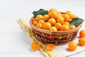 Wall Mural - Ripe yellow cherry plums with leaves on white wooden table, closeup
