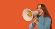 © Iryna - Young woman enthusiastically speaking into a megaphone against a bright orange background during a spirited rally or event