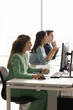 © fizkes - Group of three customer call services representatives sitting in modern co-working office, wearing headsets and working on desktop computers, communicating with clients, providing technical support