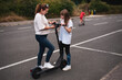 © Мар'ян Філь - Two individuals engage with an electric scooter on outdoor pavement while one tries it out. Both seem actively immersed in learning and experimenting with the scooter