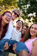 © CarlosBarquero - Vertical. Five cheerful multi-ethnic students are lifting their friend, laughing and having fun together in a park, enjoying their free time and friendship