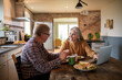© Marko Geber - Senior couple enjoying breakfast together while talking at kitchen table with laptop