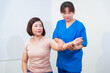 © M+Isolation+Photo - Young Asian nurse assisting middle-aged female patient on a couch doing physical therapy, focusing on muscle strengthening, rehabilitation, stretching,shoulder pain management in healthcare facility