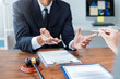 © amnaj - Lawyer explaining insurance policy details to client using hand gestures, with gavel and documents on desk