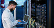 © peopleimages.com - Man, laptop and typing for inspection in server room, hardware and programming for IT solution at company. Person, cybersecurity and assessment with computer, coding and update software for system