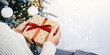 © guguart - Festival background. Giving gifts to loved ones during the Christmas holiday with a second hand holding a gift box wrapped in a red ribbon in a celebration concept