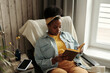 © TrueFrame Collective - Horizontal high angle portrait shot of young African American woman wearing casual outfit relaxing in chair at home reading novel