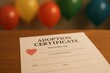© Maryia - Adoption Day certificate on desk with child crayon heart drawing beside it, festive balloons blurred in background, symbolic hopeful moment of love, family bond, rescue success, joyful new beginning