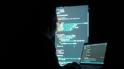 Male programmer works late at night with green code reflecting on his lenses, focusing on software development, coding, and cybersecurity analysis in dark room. 
