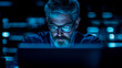 © sommersby - Intense bearded man with glasses reflecting blue screen light, deeply focused on his laptop in dark, high-tech environment with glowing data servers