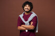© ViDi Studio - Young smiling happy cheerful Indian man he wear purple t-shirt sweatshirt tied over shoulders casual clothes hold hands crossed folded look camera isolated on plain brown background Lifestyle concept
