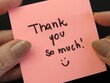 © Verediana Hille - Woman hands holding pink note with the expression 'Thank you so much' and a smile on black background. Thank you card.