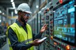 © Viktor - African engineer in hard hat and safety vest uses tablet to control electronic circuit. Industrial plant setting with working machinery highlights manufacturing, technology, and skilled labor.